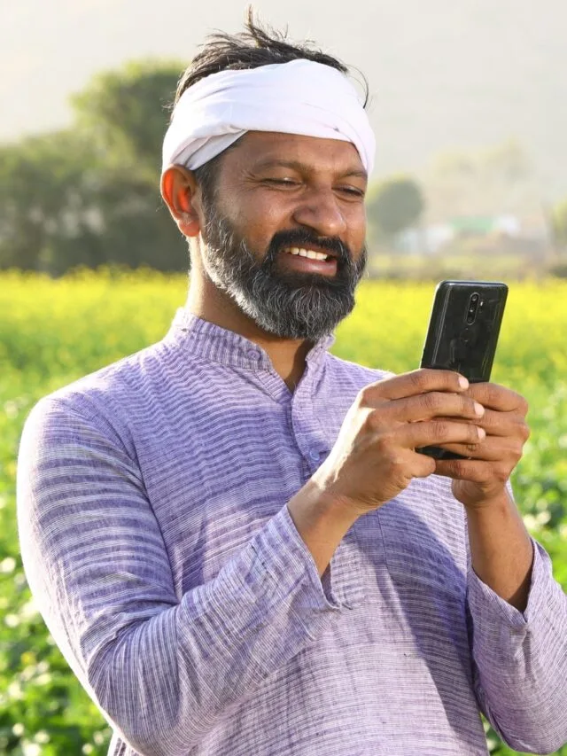 Happy Indian farmer smiling in a lush green field with a mobile, symbolizing prosperity from the PM Kisan Yojana.